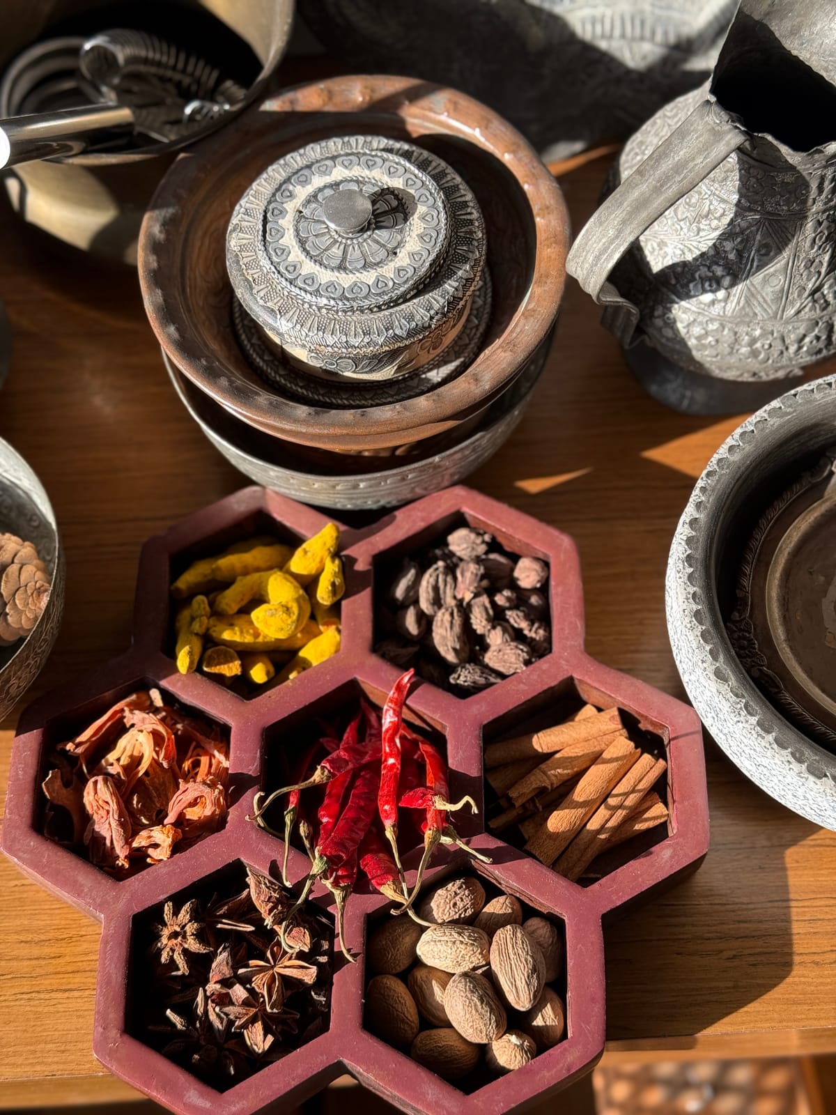 An assortment of whole Indian spices including star anise, cardamom, cinnamon, and dried chilies arranged in a hexagonal masala box with antique spice grinders
