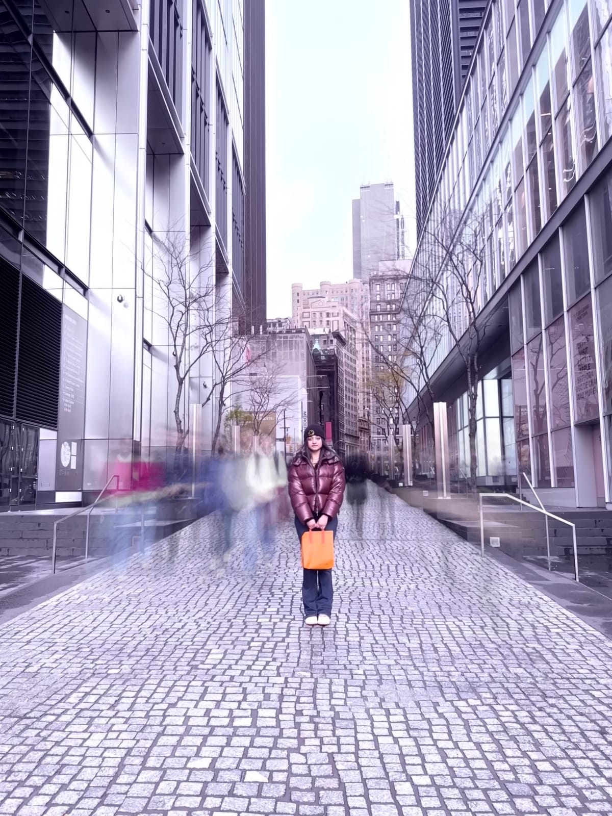 Tanvi standing alone on a cobblestone pedestrian street between glass skyscrapers in downtown Toronto in winter