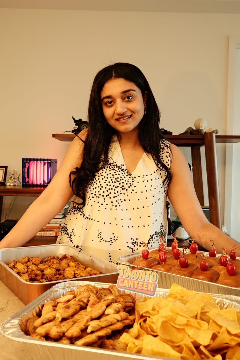 Tanvi smiling behind a table of Toronto Canteen packaged food trays at a pop-up event