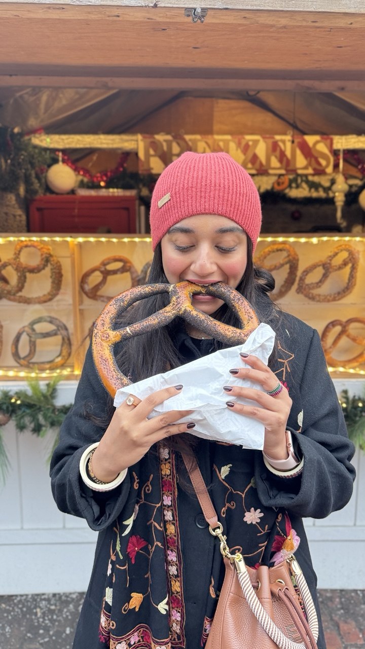 Chef Tanvi Mahajan eating a giant pretzel at a winter market in Toronto